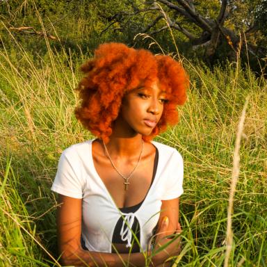 Laura sitting in a field of long grass in front of a tree